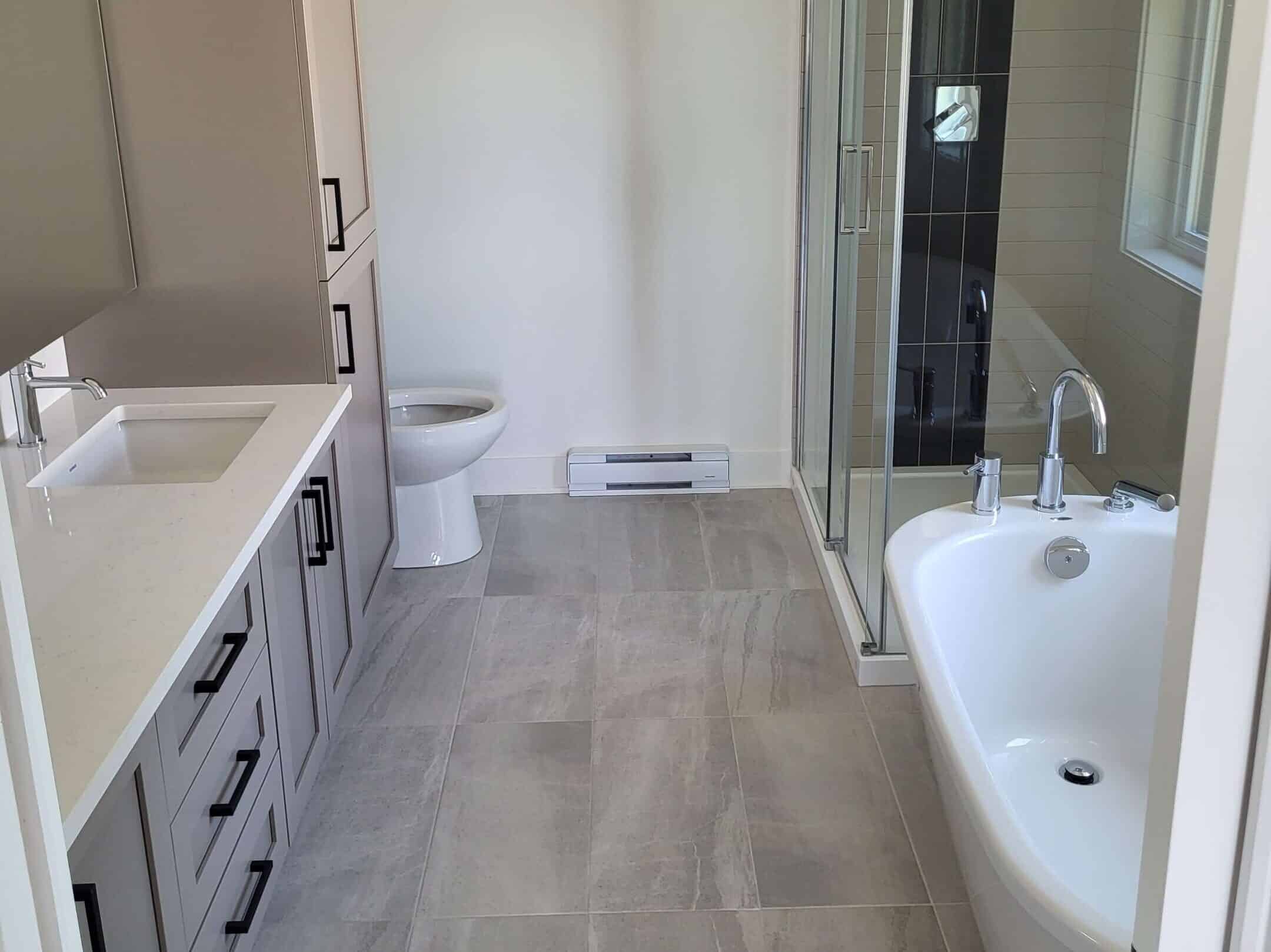 Salle de bain moderne d’une maison neuve au Québec avec douche vitrée, bain autoportant et comptoir en quartz, exemple de finition haut de gamme signée constructeur résidentiel.