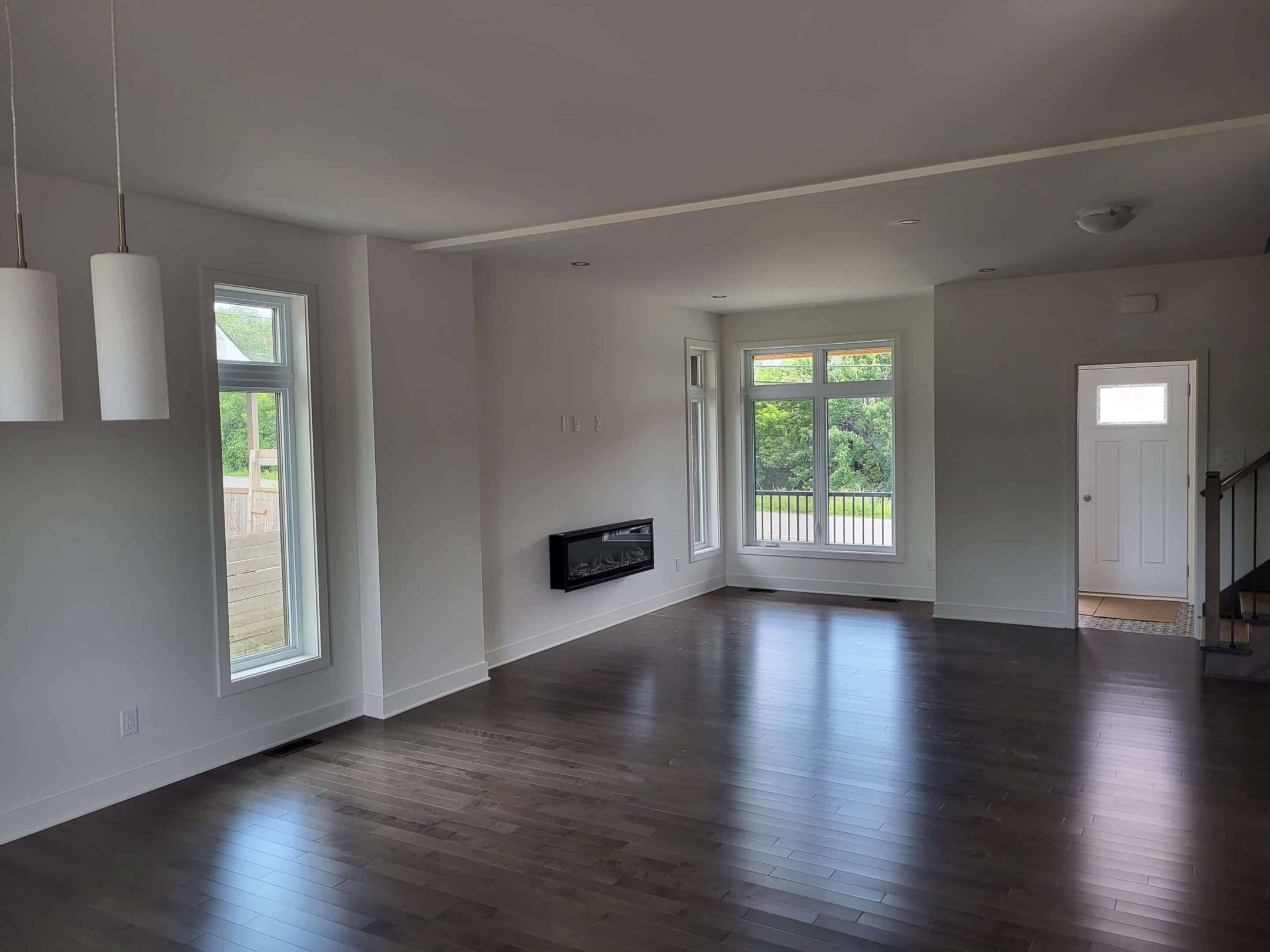 entrepreneur en construction pointe aux trembles Salon lumineux d’une maison neuve au Québec avec plancher de bois foncé, grandes fenêtres et foyer mural, exemple de design contemporain signé constructeur résidentiel.